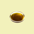 Ciotolina di vetro con olio di avocado dorato su sfondo giallo chiaro