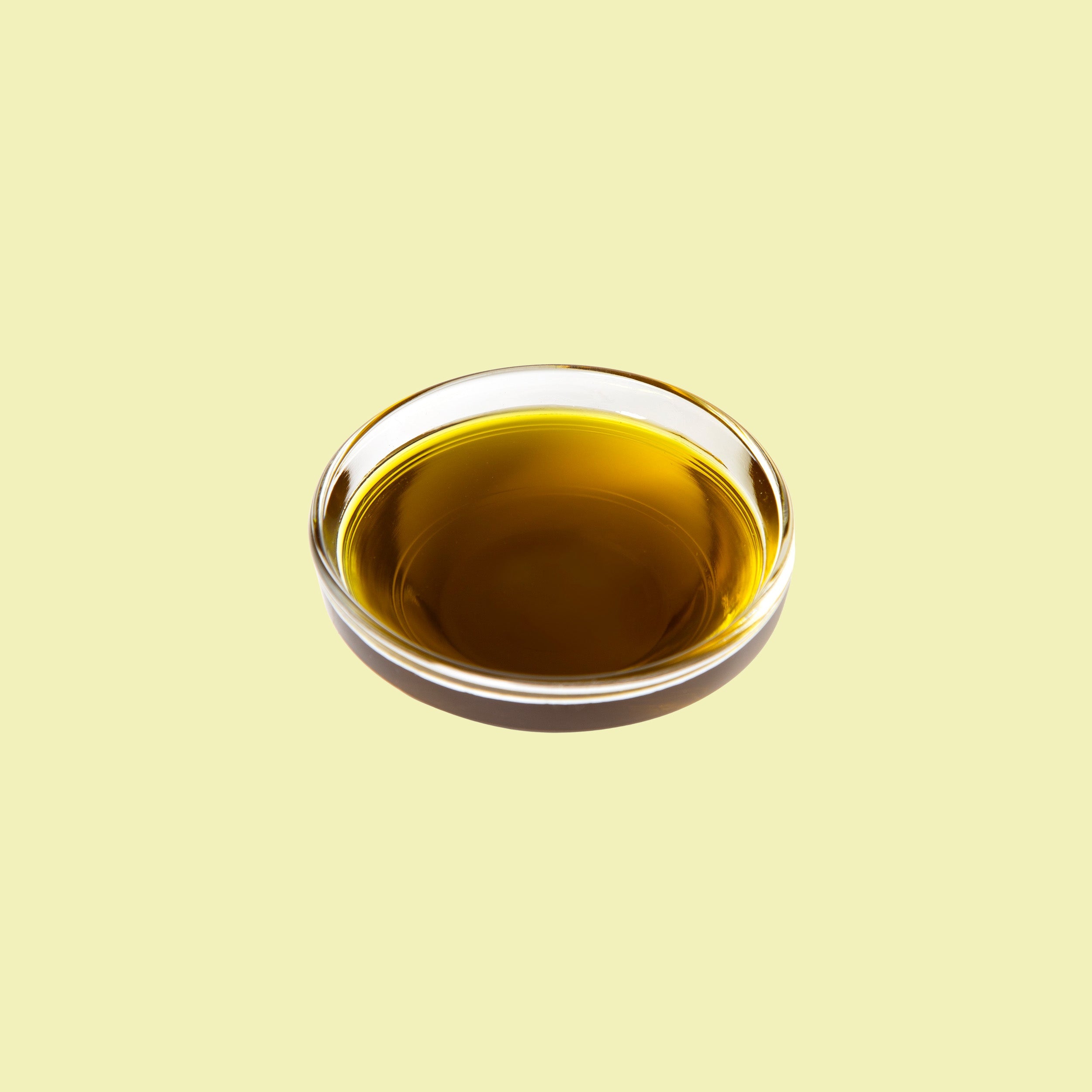 Ciotolina di vetro con olio di avocado dorato su sfondo giallo chiaro